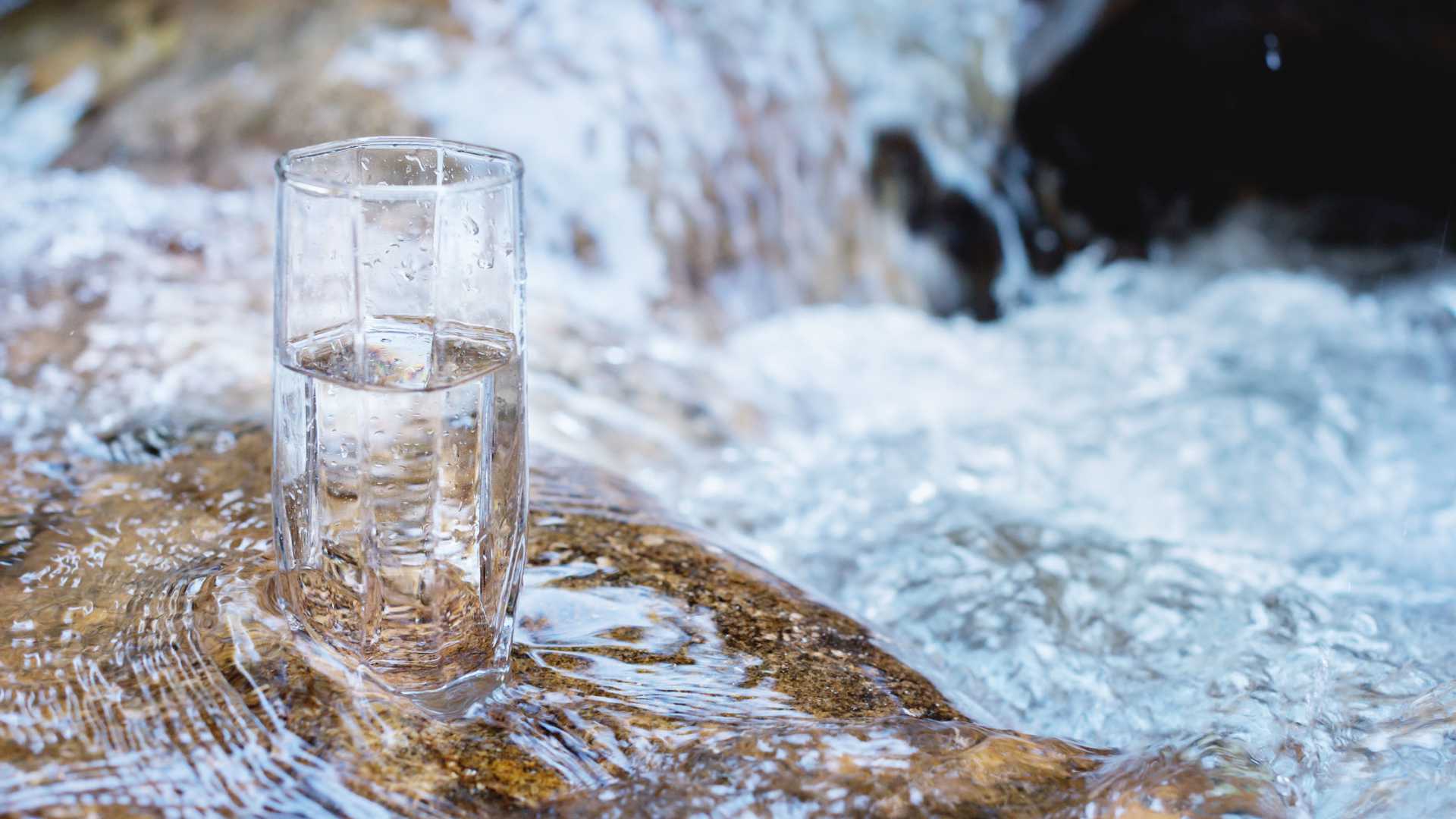 Warum ist Wasser nass? Wasserglas steht auf Steinen an einem kleinen Wasserfall