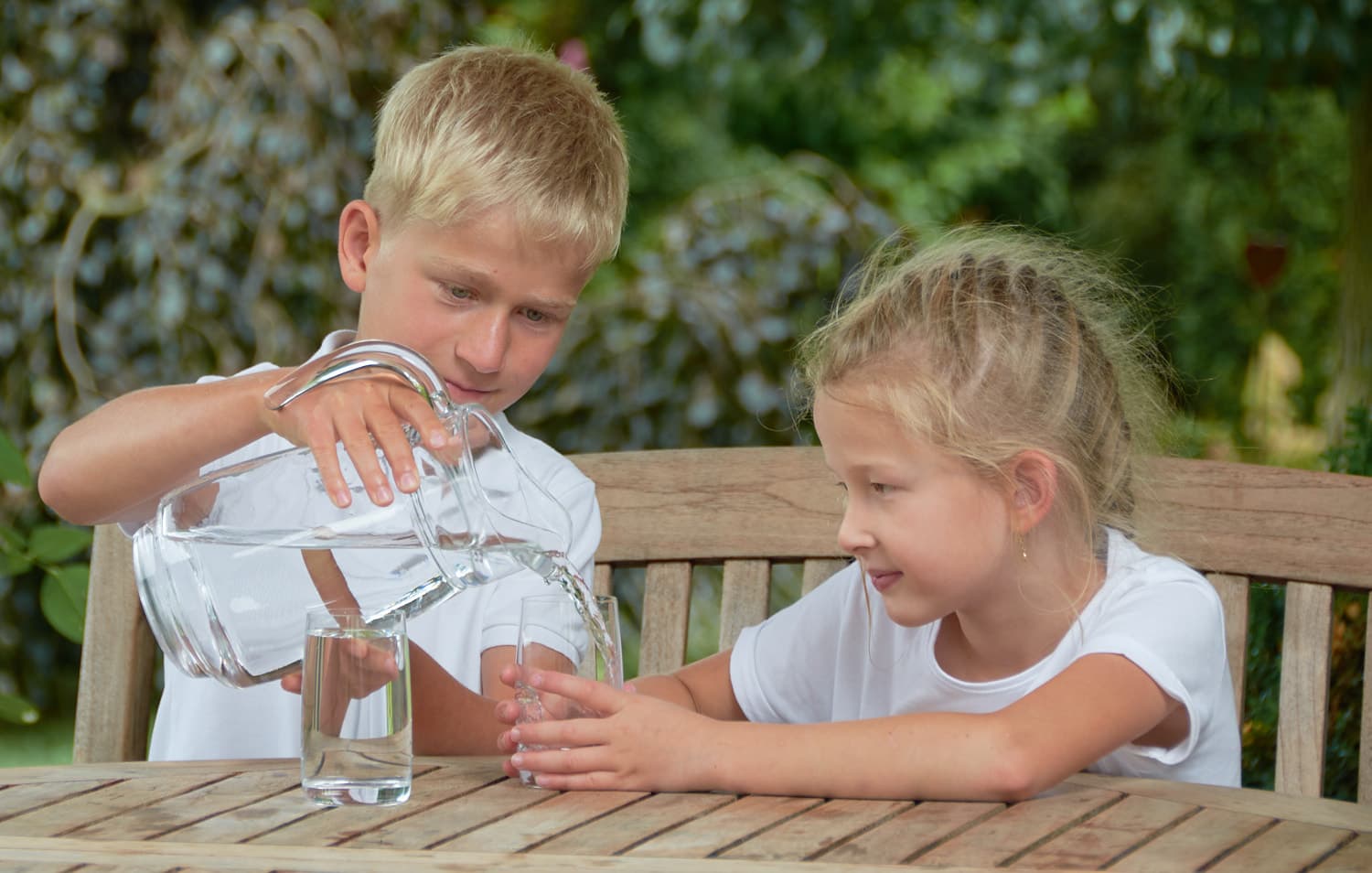 Junge gießt Mädchen im Garten ein Glas sauberes Wasser ein