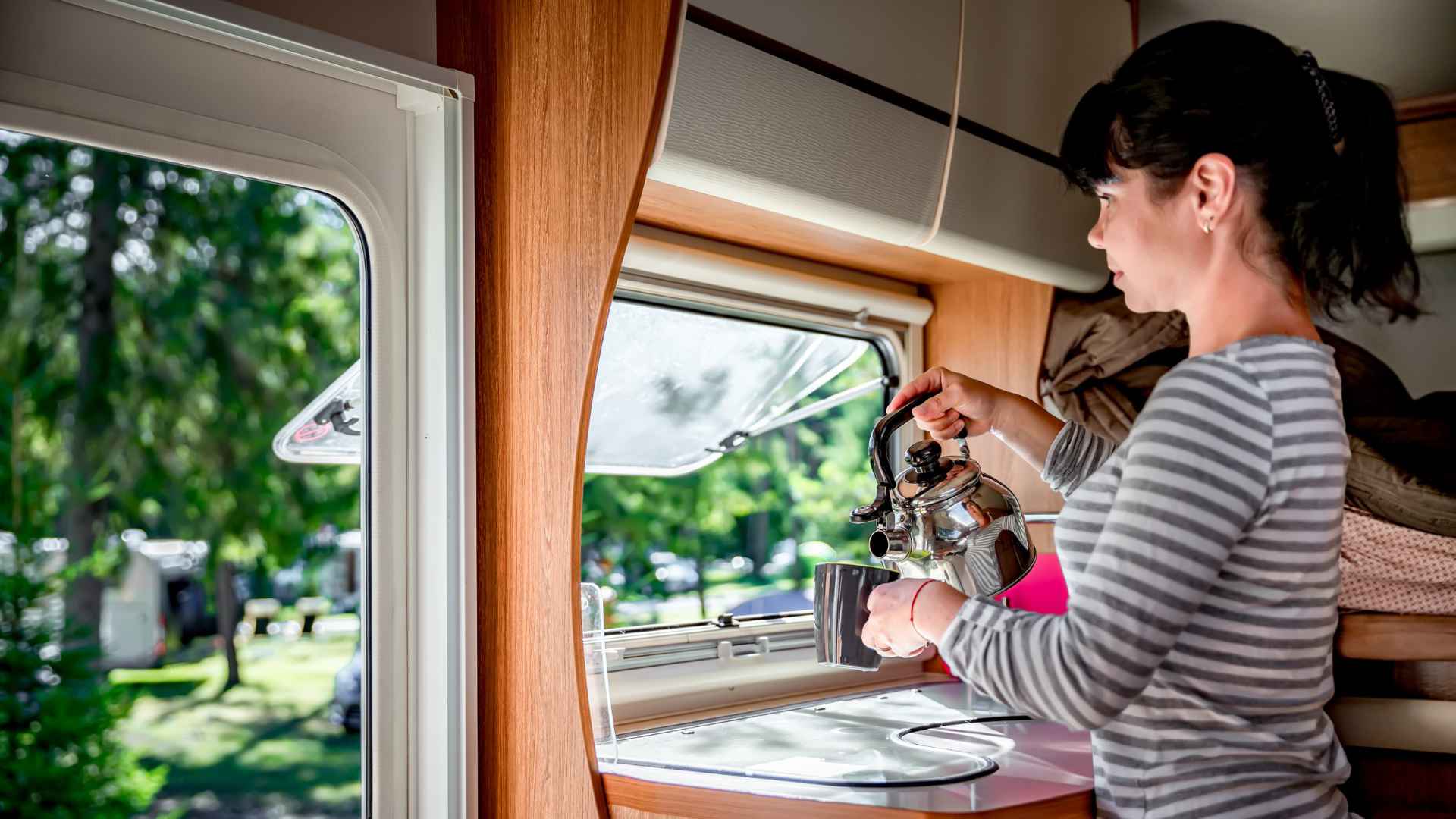 Kann man das Wasser aus dem Wohnmobil trinken? Junge Frau auf dem Campingplatz gießt sich heißes Wasser in die Tasse