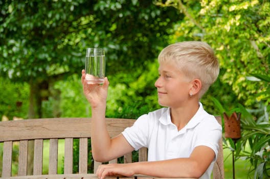 junge schaut sich ein Glas Wasser im Garten an