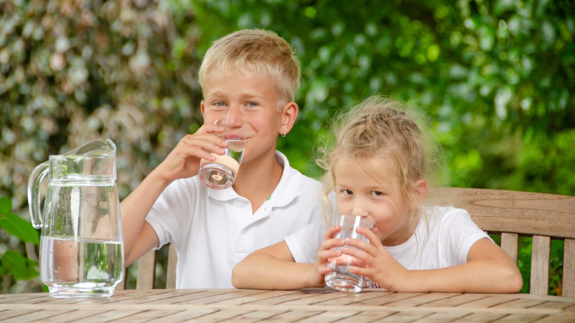 Zwei Kinder trinken im Garten sauberes Wasser aus einer VISION AQUA Umkehrosmoseanlage