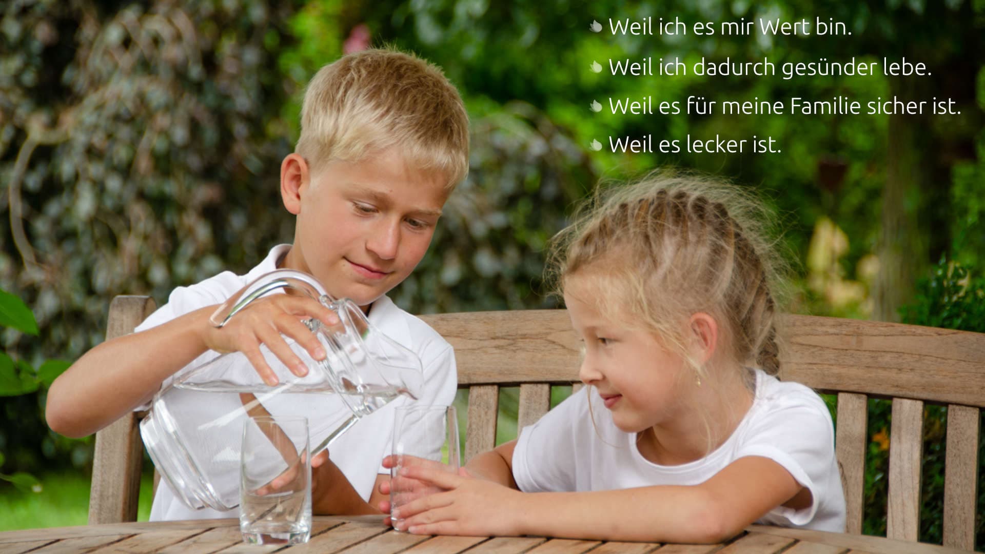 Junge gießt einem Mädchen ein Glas sauberes Wasser im Garten ein