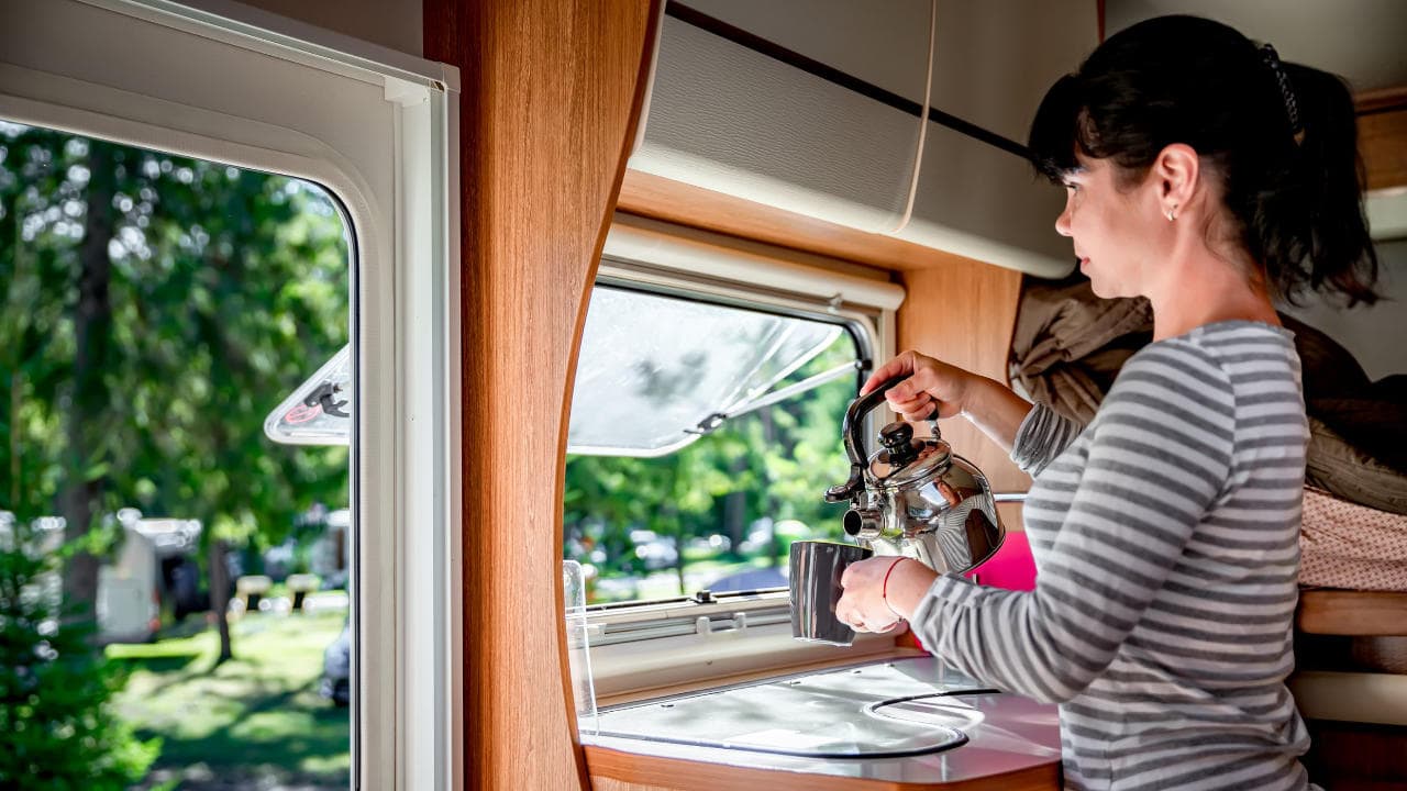 Junge Frau auf dem Campingplatz gießt sich heißes Wasser in die Tasse